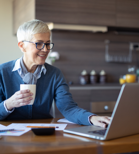 person smiling and sitting at a desk with a cup of coffee while working on a laptop.